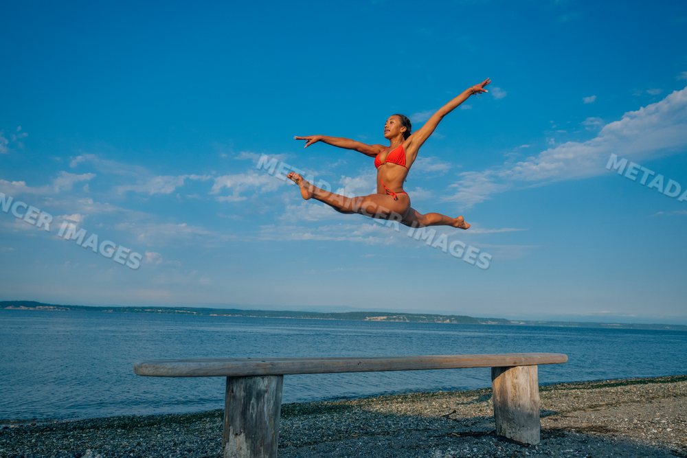Woman in red swimsuit performing an athletic jump above a bench