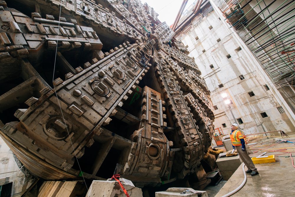 Two construction workers wearing safety helmets and vests inspect a massive tunnel boring machine at an underground construction site, the tunnel boring machine, drilling, USA.