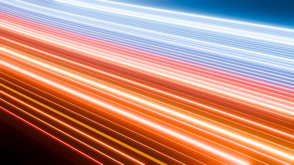 Colorful light trails of red, orange, white, and blue streak across a nighttime road in a long-exposure photograph.