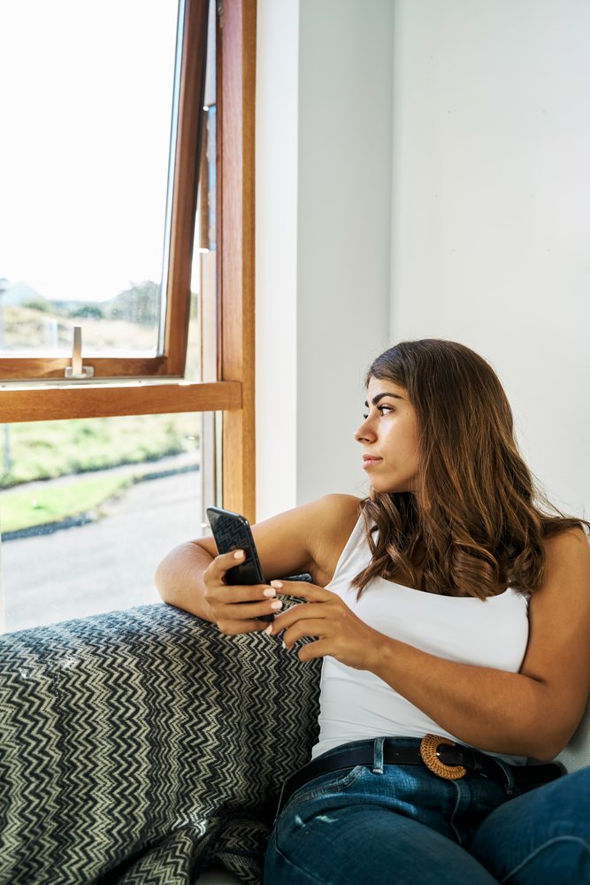 A white woman sitting on a couch uses a smartphone