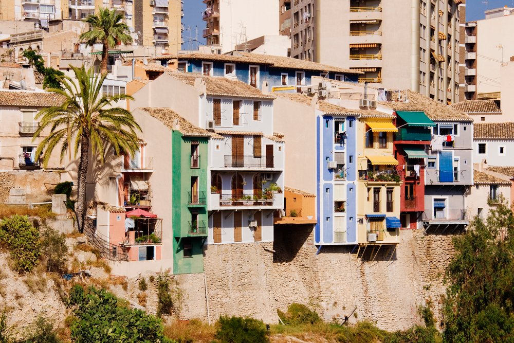 Colorful apartment buildings with balconies and palm trees along a stone wall in an urban residential area of, Alicante, Spain.
