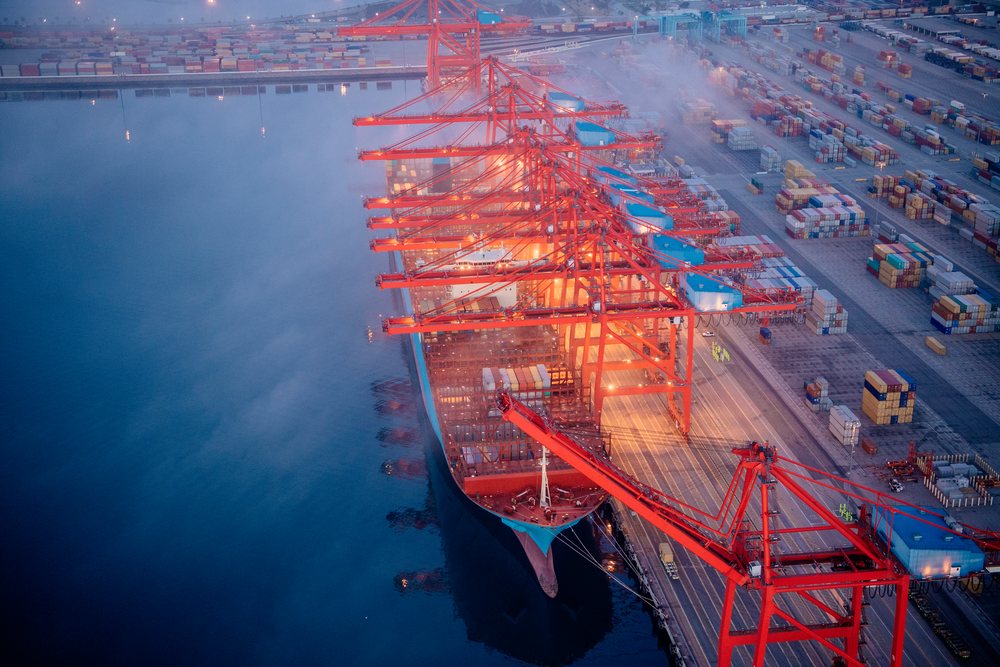 Container ship being loaded with cargo containers by red container cranes at the port in Long Beach, lifornia in foggy dusk conditions, Port of Long Beach, CA, USA.