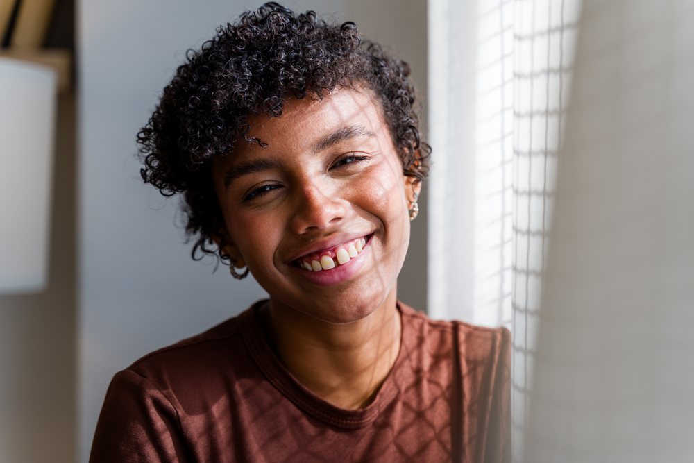 Woman with curly hair smiles indoors near a window with natural light, Spain.
