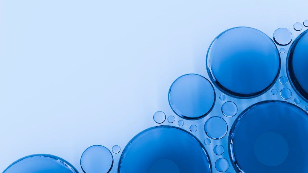 Blue liquid bubbles clustered on a smooth surface showing surface tension and round shapes in macro detail.