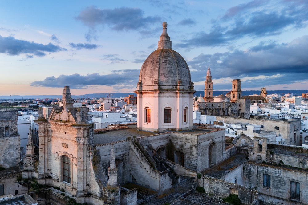 Sunrise illuminates a historic cathedral dome and stone rooftops in the Mediterranean town of, Monopoli, Puglia, Italy.