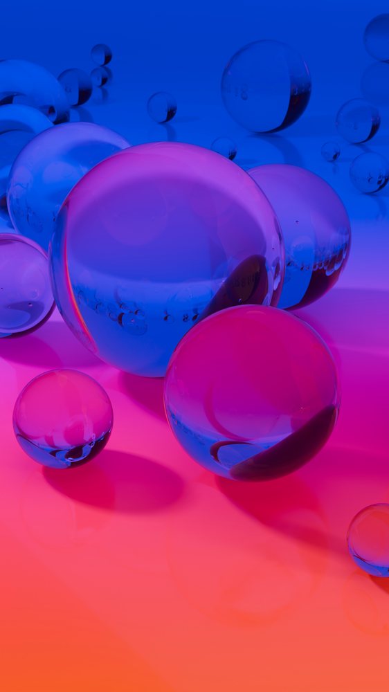 Cluster of transparent glass spheres with blue and pink reflections on a reflective surface under gradient lighting.