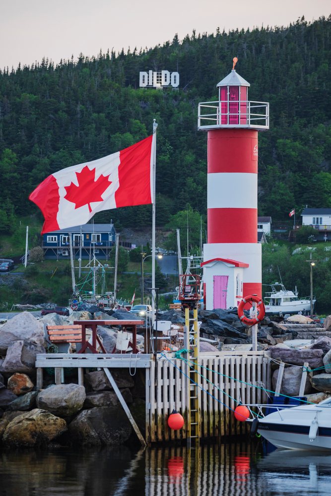 Red and white striped Lighthouse on harbor dock with Canadian flag flying and Dildo Sign on forested hillside in Newfoundland, Landscape, Cityscape, Lifestyle, Newfoundland & Labrador, Canada.