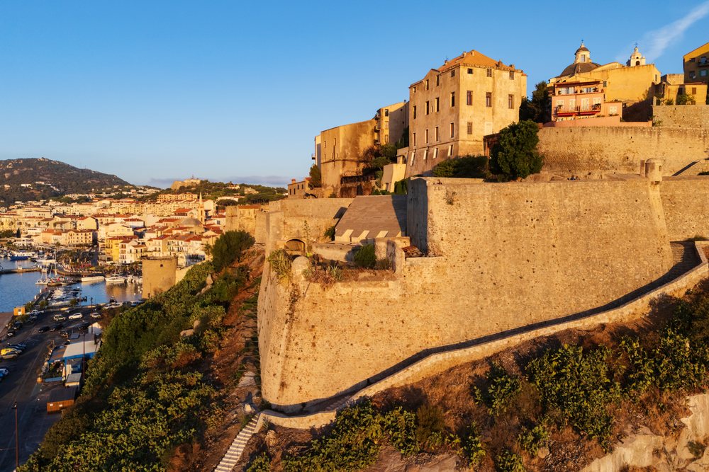 Historic stone-walled Citadel and Harbour with marina and church dome, glowing in golden sunset light, Travel Photography, Calvi, Corsica, France.