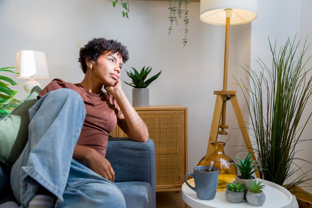 Young woman sitting thoughtfully on a blue sofa at home.