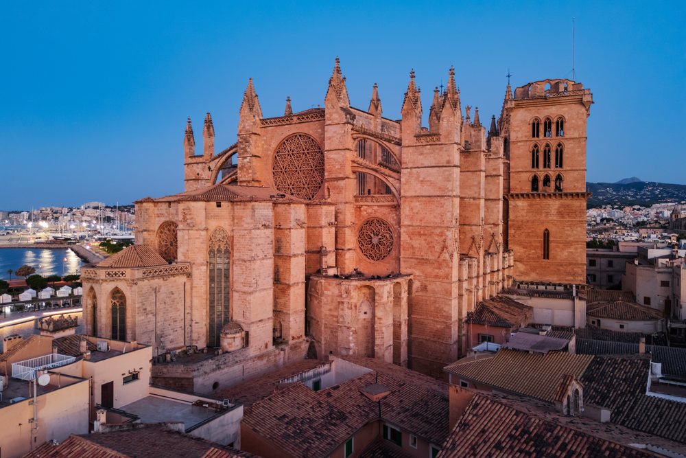 Gothic Cathedral in Palma de Mallorca illuminated at dusk with surrounding rooftops and harbor, Landscape, Lifestyle, Balearic Islands, Spain.