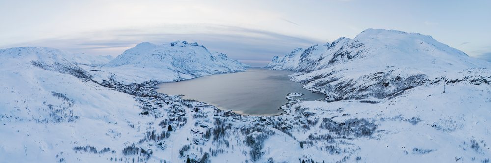 Snow-covered mountains surround Ersfjorden fjord at sunset with a small village at the water's edge, Landscape, Ersfjordbotn, Norway.