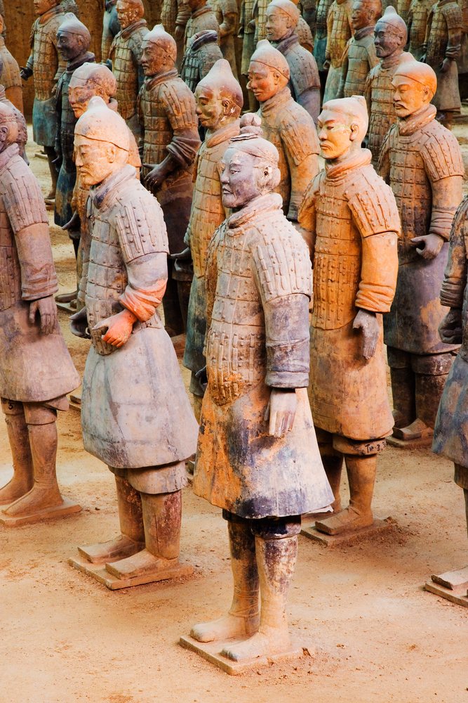 Multiple terracotta warrior statues in ancient armor stand in formation at an indoor museum site, Shaanxi Province, China.