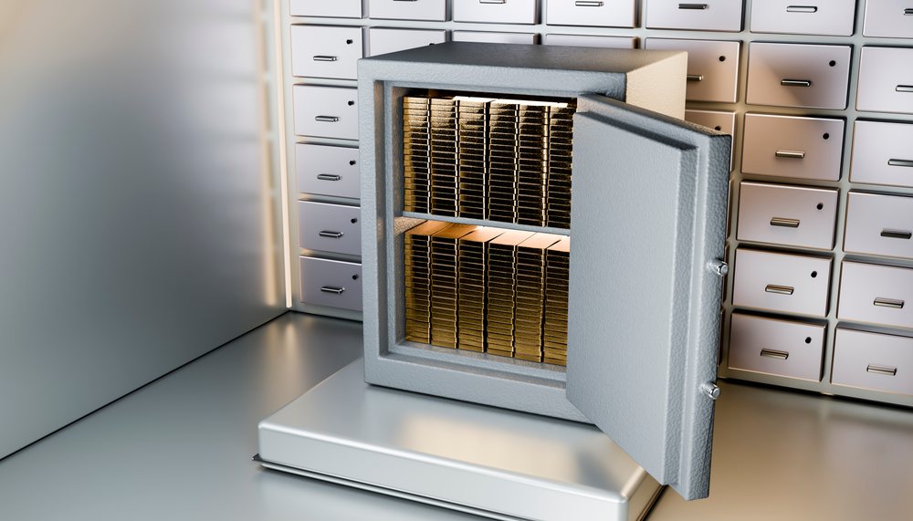 Open metal safe filled with stacked gold bars inside a vault room with metal lockers in the background.