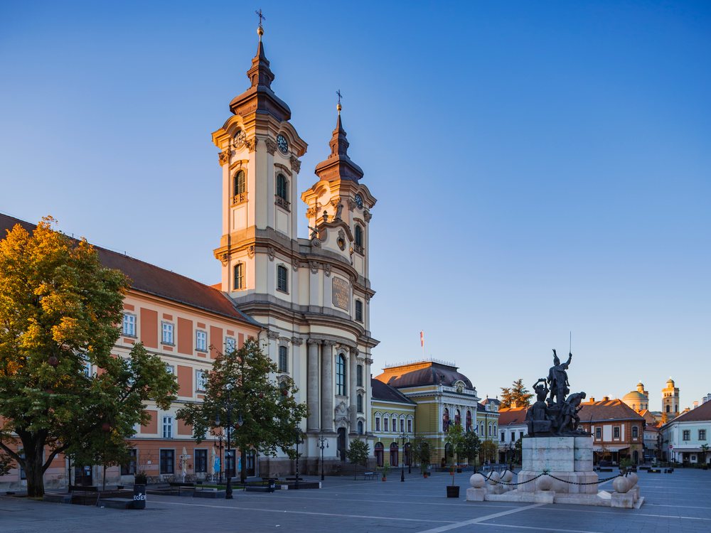 The Minorite Church with twin towers and statue on a stone pedestal at Sunrise under a clear sky, Cityscape, Eger, Hungary.