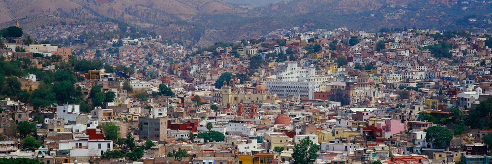 Panoramic daytime view of colorful hillside residential buildings with mountain terrain in the background in a dense urban area.