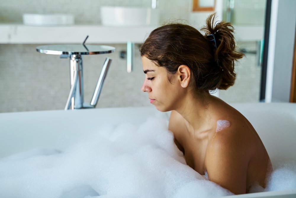 A woman relaxes in a bubble bath surrounded by foam in a modern bathroom in the, Maldives.