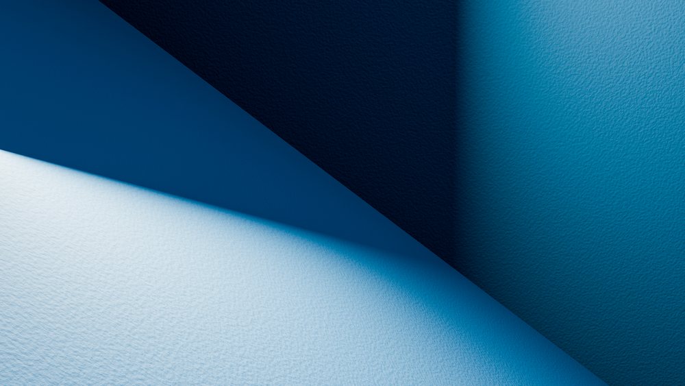 Blue wall with textured surface illuminated by angled light casting angular geometric shadows creating a cross-shaped pattern.