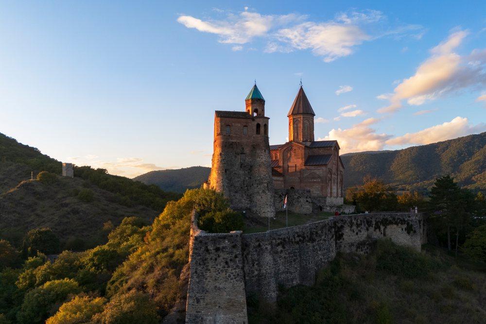 Gremi Monastery, a historic stone fortress with twin towers, perched on a hilltop at Sunset with surrounding mountains and clouds, Sighnaghi, Georgia.