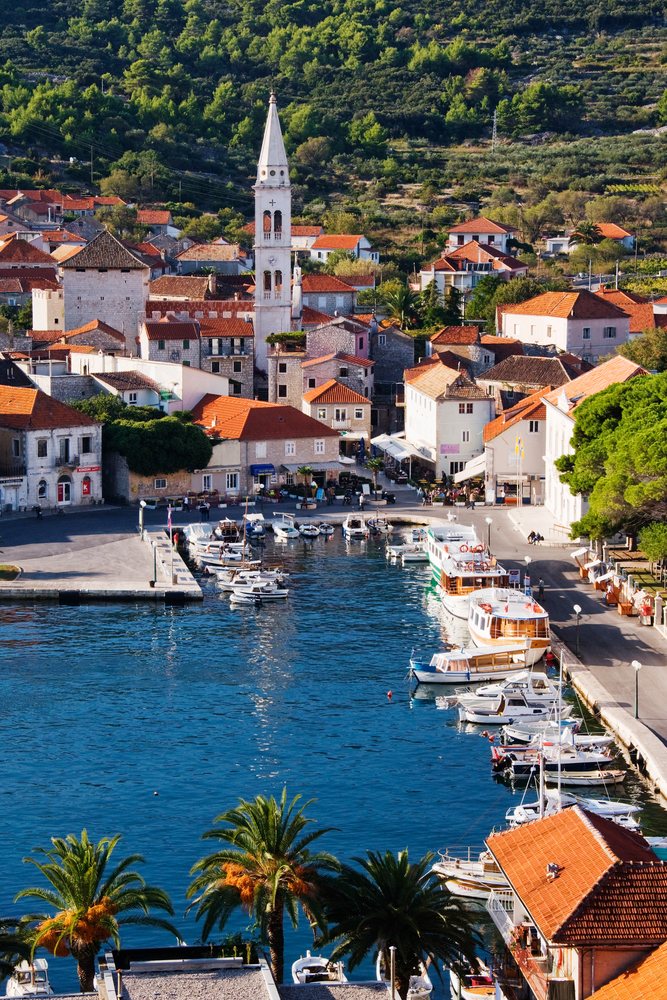 Harbor of Hvar Island shows boats docked alongside a coastal town with a prominent church tower and Mediterranean architecture, Croatia.