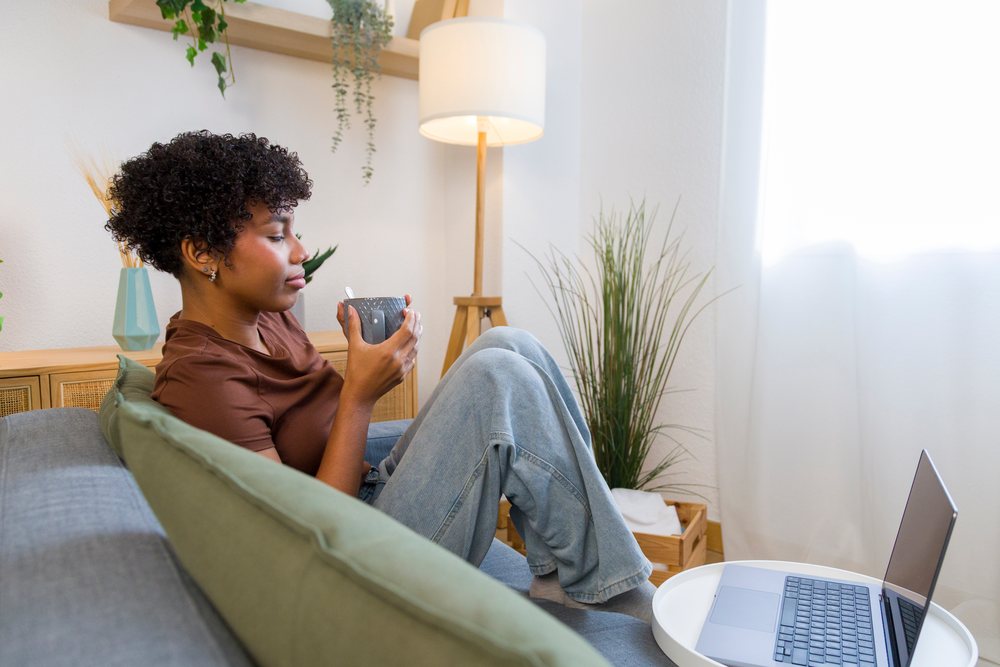 Young woman sitting on sofa drinking from cup in cozy living room.
