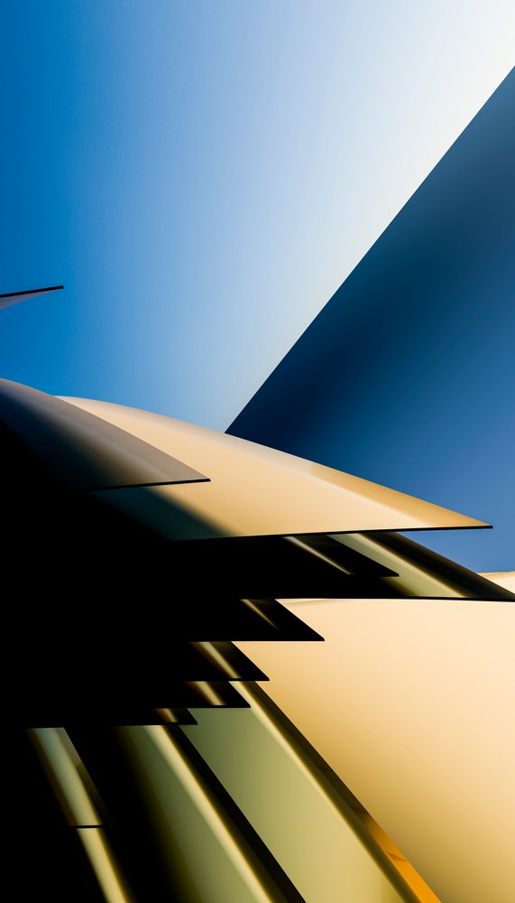 Modern urban building with glass facades and geometric shapes under clear blue sky reflecting sunlight.