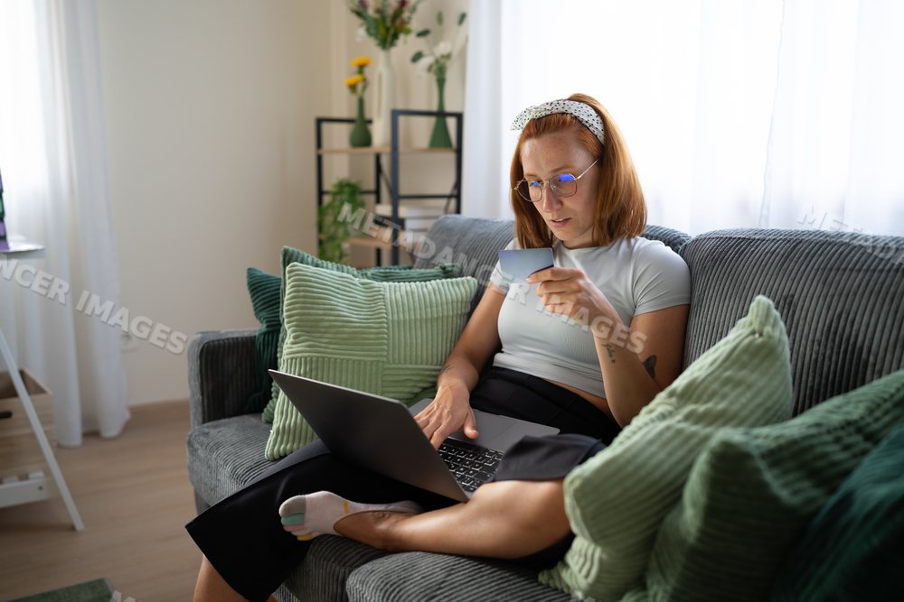 A white woman shopping online with a credit card and laptop at home