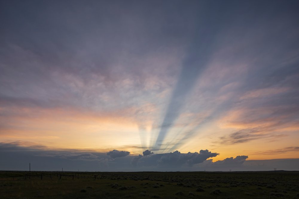 Anti-crepuscular rays appear over a cloudy Sunset sky above a grassy field in the Great Plains, USA's Tornado Alley during storm chasing.