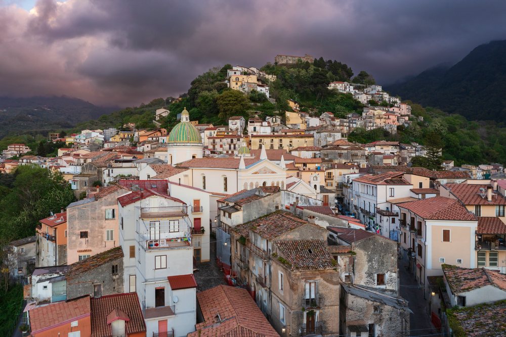 Aerial view at dusk of the hill town of Nocera Terinese with terracotta-roofed buildings and mountains in the background, Calabria, Italy.