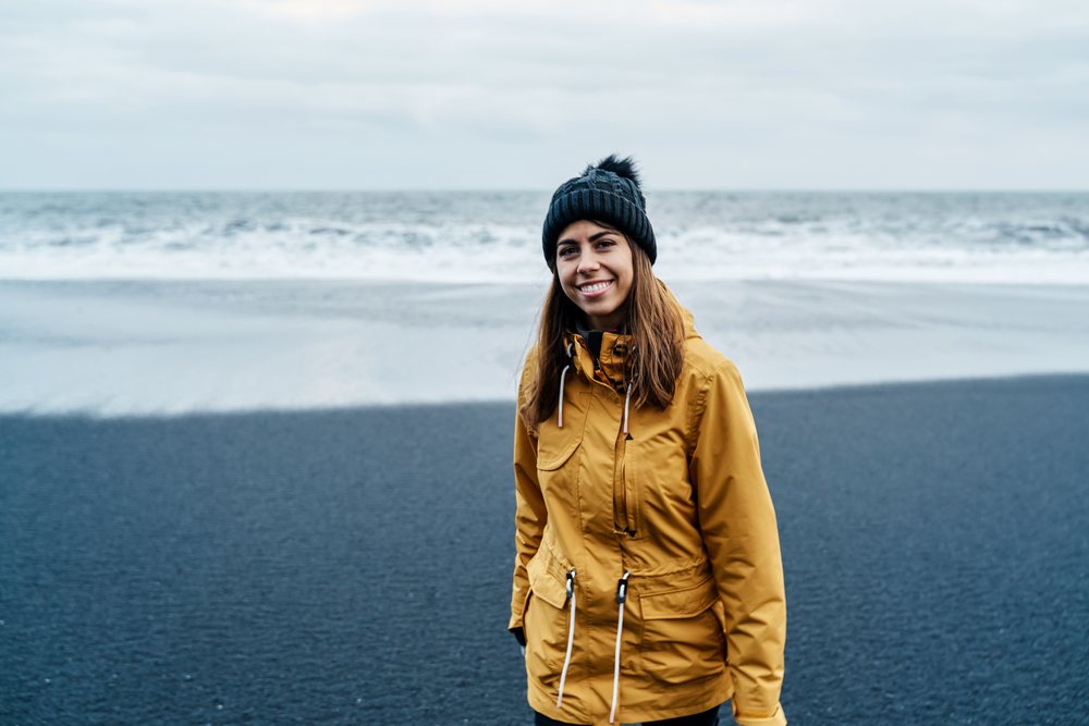 Smiling white woman in yellow jacket standing on black sand beach