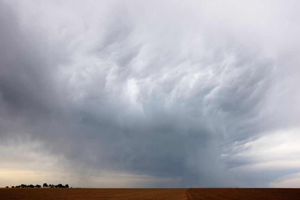 Storm clouds hover over a flat, open field, signaling severe weather conditions approaching the area, Texas, USA.