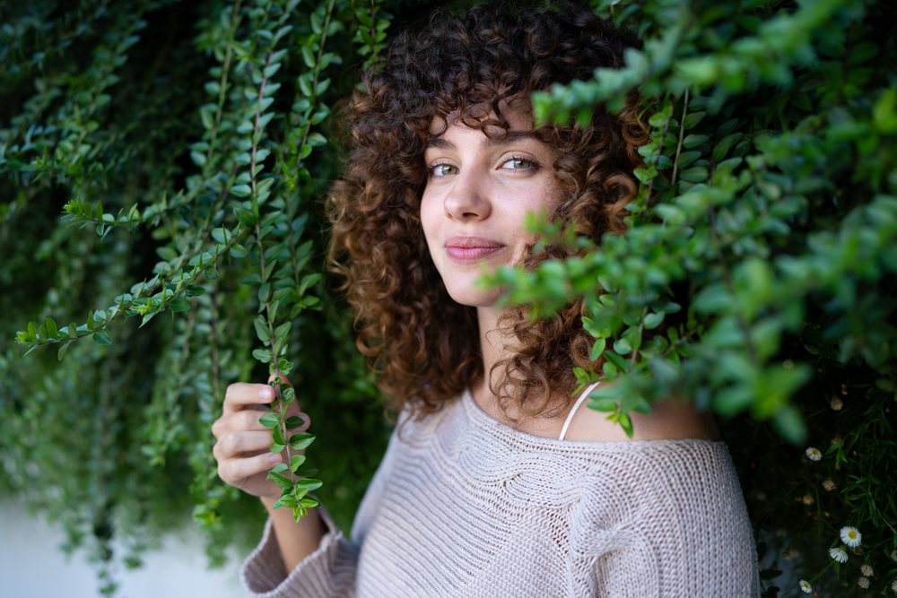Woman with curly hair smiling outdoors holding green leaves, home story, influencer, Spain.