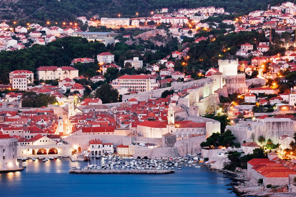 Old city of Dubrovnik with illuminated medieval stone walls and harbor boats, Dawn, Croatia.