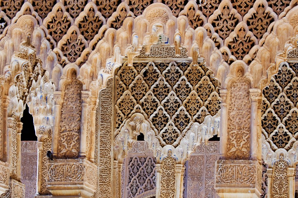 Close-up of intricately carved stone arches with Islamic ornamental patterns and Arabic calligraphy at the Alhambra, Granada, Spain.