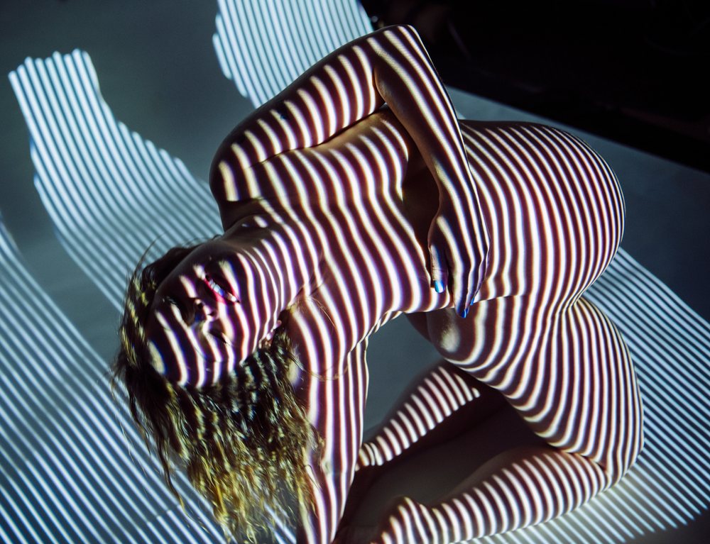 Pregnant woman in studio posed with striped light projection creating an artistic shadow pattern on her nude body, pregnancy.