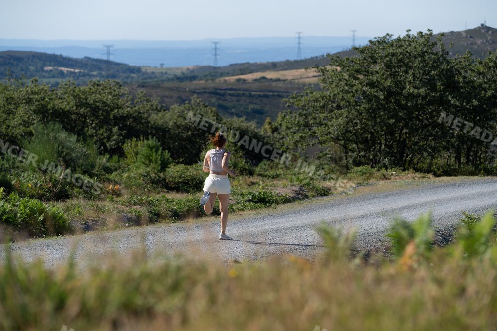 A white woman runs on a gravel trail surrounded by nature in Galicia