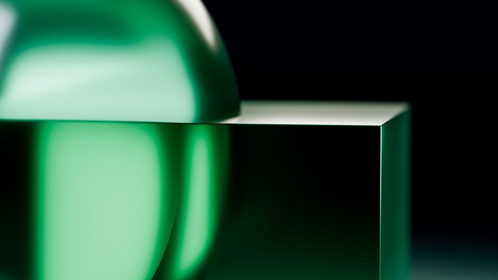 Green glass sphere resting on a reflective glass block in a minimalist abstract composition with smooth glossy surfaces.