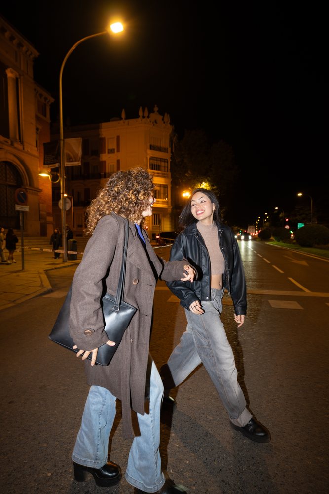 Two women holding hands and walking on a city street at night, Madrid, Spain.