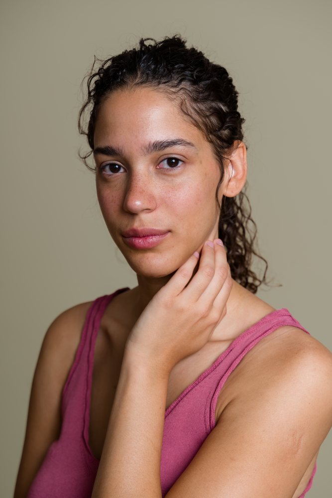 Portrait of a woman with curly hair touching her neck against a neutral studio background, beauty shoot, Spain.
