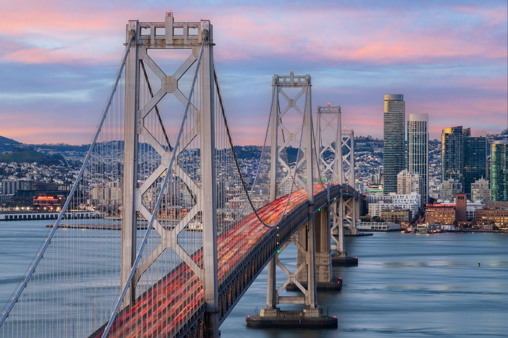 Bay Bridge with traffic illuminated by vehicle lights at Sunrise against the San Francisco skyline and waterfront, City, Cityscapes, City Life, California, USA.