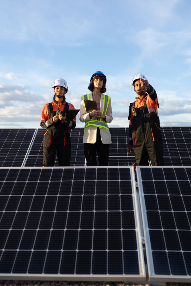Engineers wearing helmets and safety vests inspecting solar panels outdoors under a partly cloudy sky, Madrid, Spain.