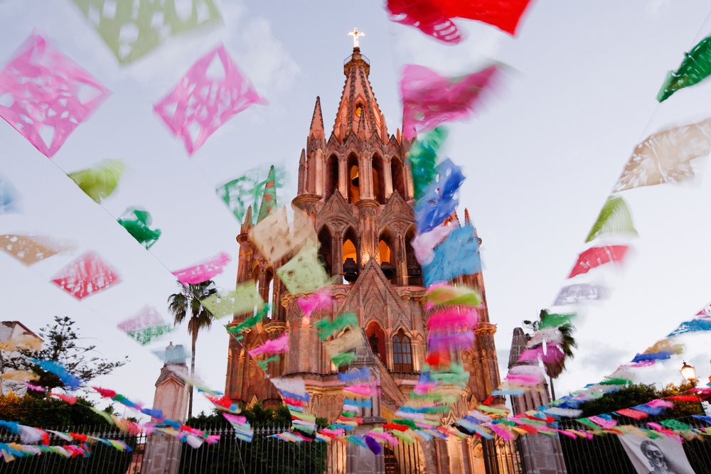 Church decorated with colorful paper banners during Day of the Dead celebrations, under an evening sky with clouds, San Miguel de Allende, Mexico.