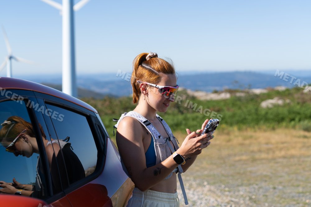 A white woman uses her smartphone beside a car with wind turbines