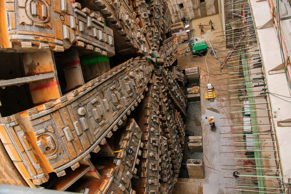 Two workers inspect a large tunnel boring machine drilling underground on a construction site, USA.