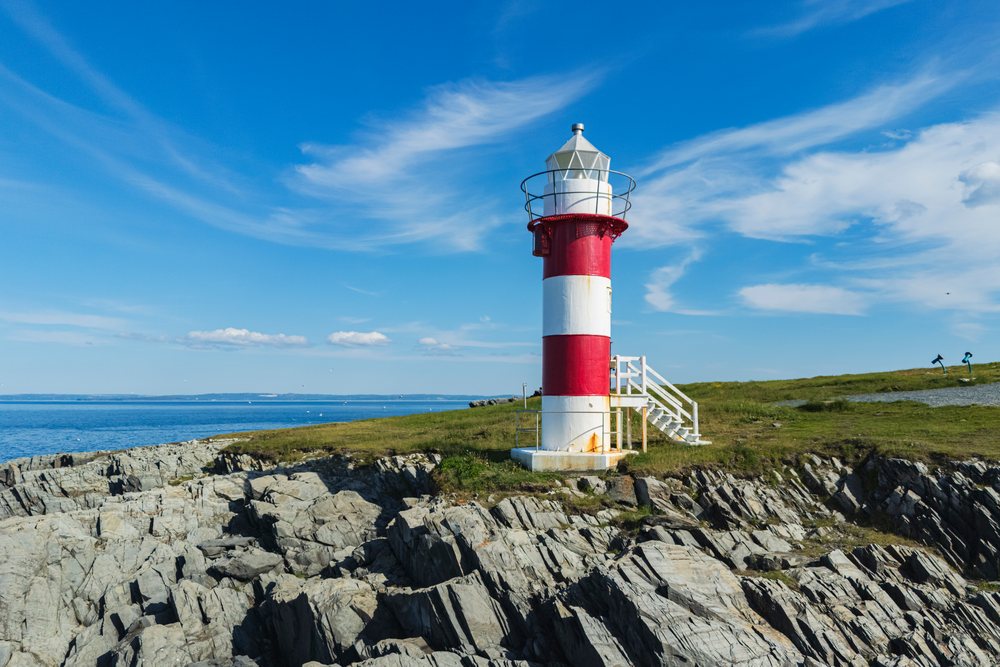 Red and white striped green Point Lighthouse stands on a rocky coastline beside blue ocean water under a clear sky, Newfoundland, Landscape, Wildlife, Lifestyle, Port de Grave, Newfoundland & Labrafor, Canada.