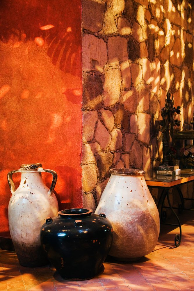 Three clay pots displayed indoors against stone and red stucco walls with sunlight casting shadows, Guanajuato, Mexico.