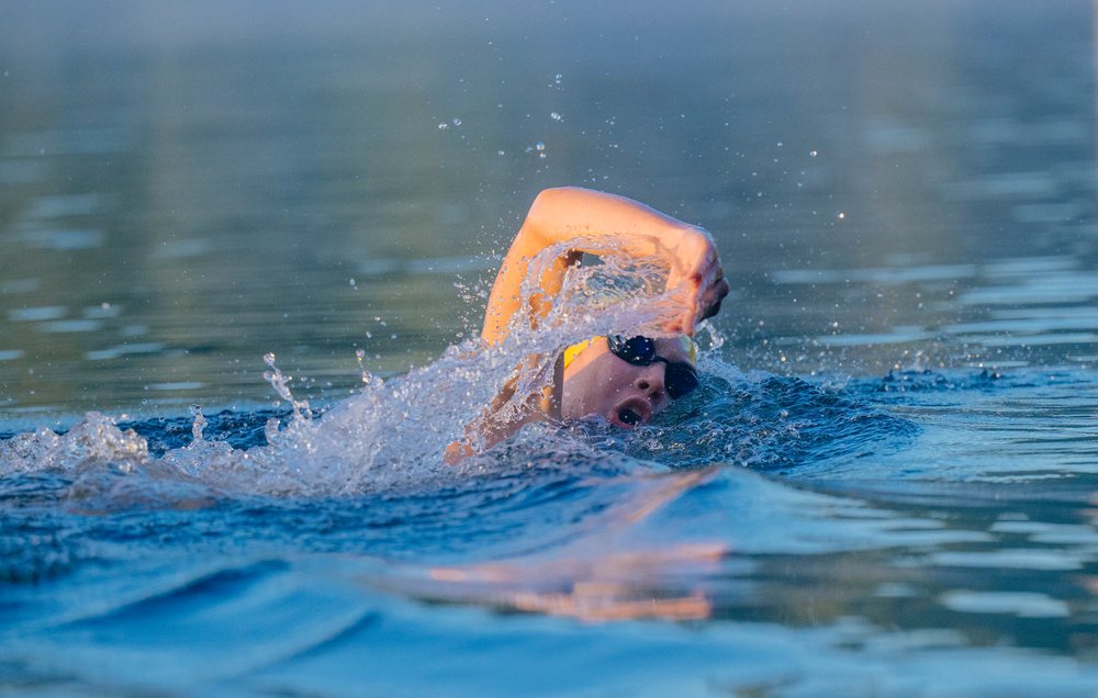 Swimmer performing the freestyle stroke in open water with splashes, wearing goggles and a swim cap, USA.