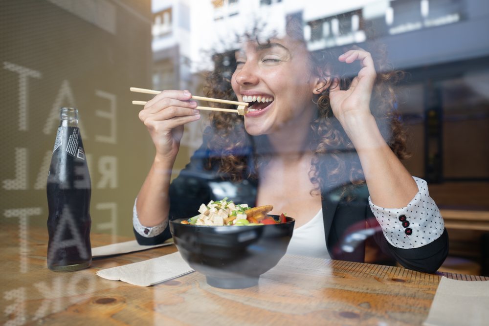 Woman eating food with chopsticks from a bowl inside a restaurant, businesswoman, traveling executive, Spain.