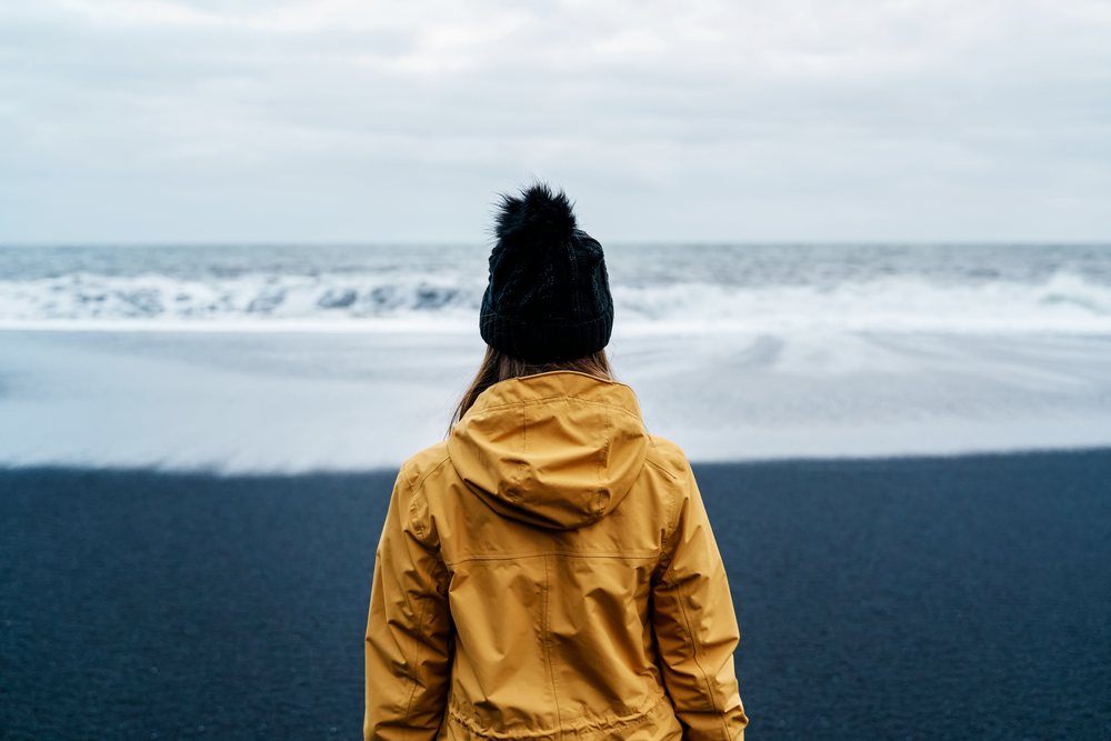 A white person in a yellow jacket looks out over the ocean