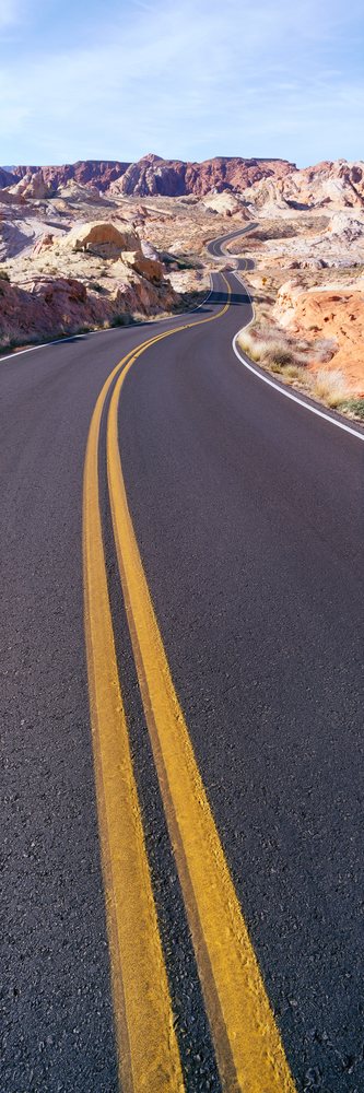 Winding asphalt road with double yellow lines curves through a rocky desert landscape, USA under a clear blue sky, Nevada.