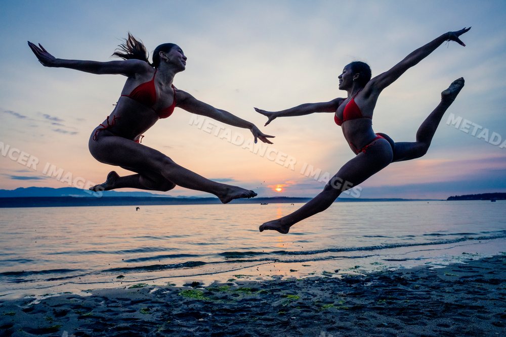 Two women perform partner acrobatics jumping on a beach